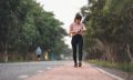 Young fitness woman runner checking time from smart watch. Young woman checking heart rate while jogging on street at dusk. Young woman looking on smartwatch her heartbeat while running in city.